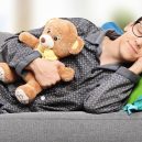 6 rad, jak správně spát - Young man in pajamas sleeping on sofa at home with teddy bear